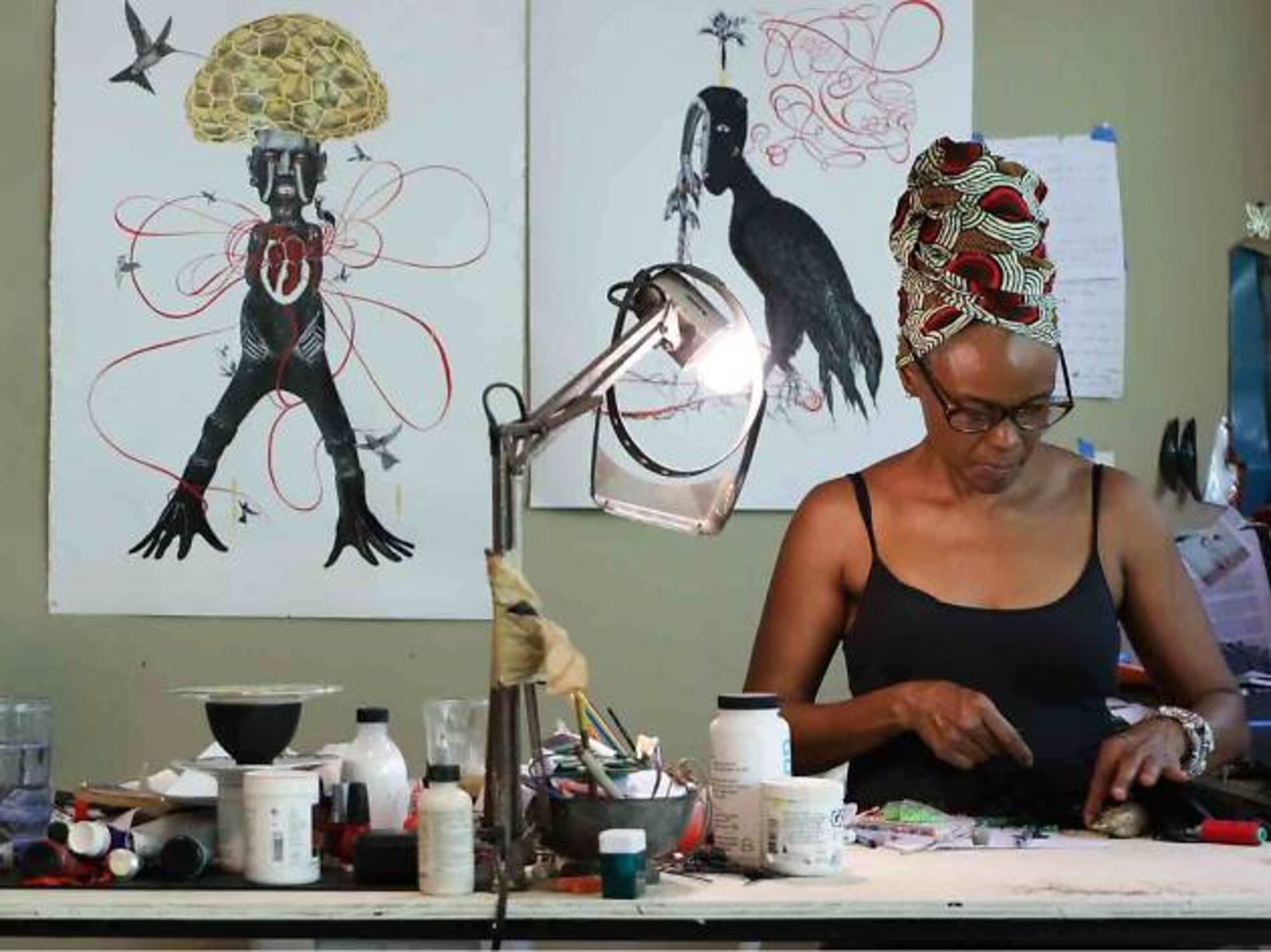 Caribbean artist working carefully at a studio table surrounded by artwork and creative materials